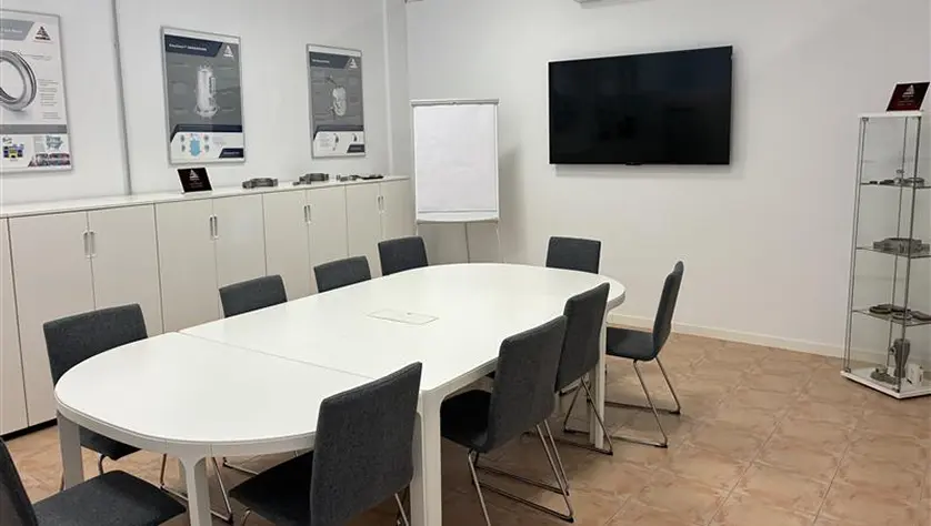 A meeting room with a long table, chairs and television screen.