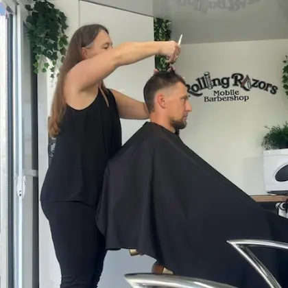 A female hairdresser cuts an employee's hair inside the Rolling Razors mobile barbershop van.